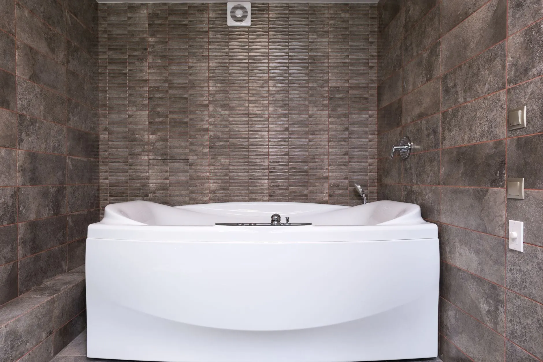 White soaking tub with a glossy refinished shell set against a stone-tiled bathroom wall